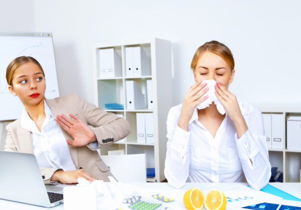 woman sneezing at her work desk into a tissue
