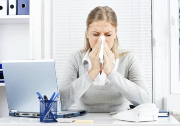 woman sneezing at her work desk into a tissue