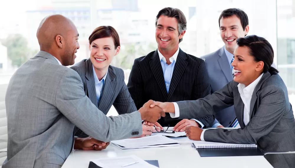 Image of a group of people in business attire sitting at a table and shaking hands.