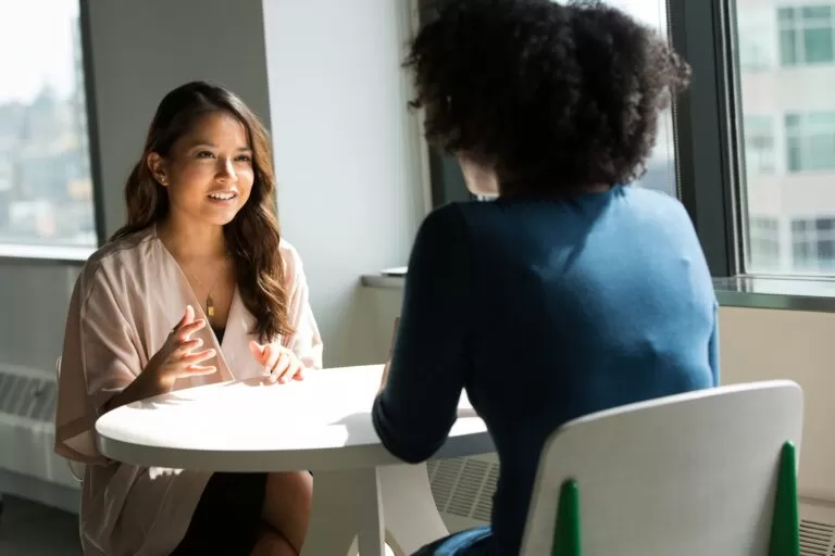 Two work colleagues talking to each other from across from the table.